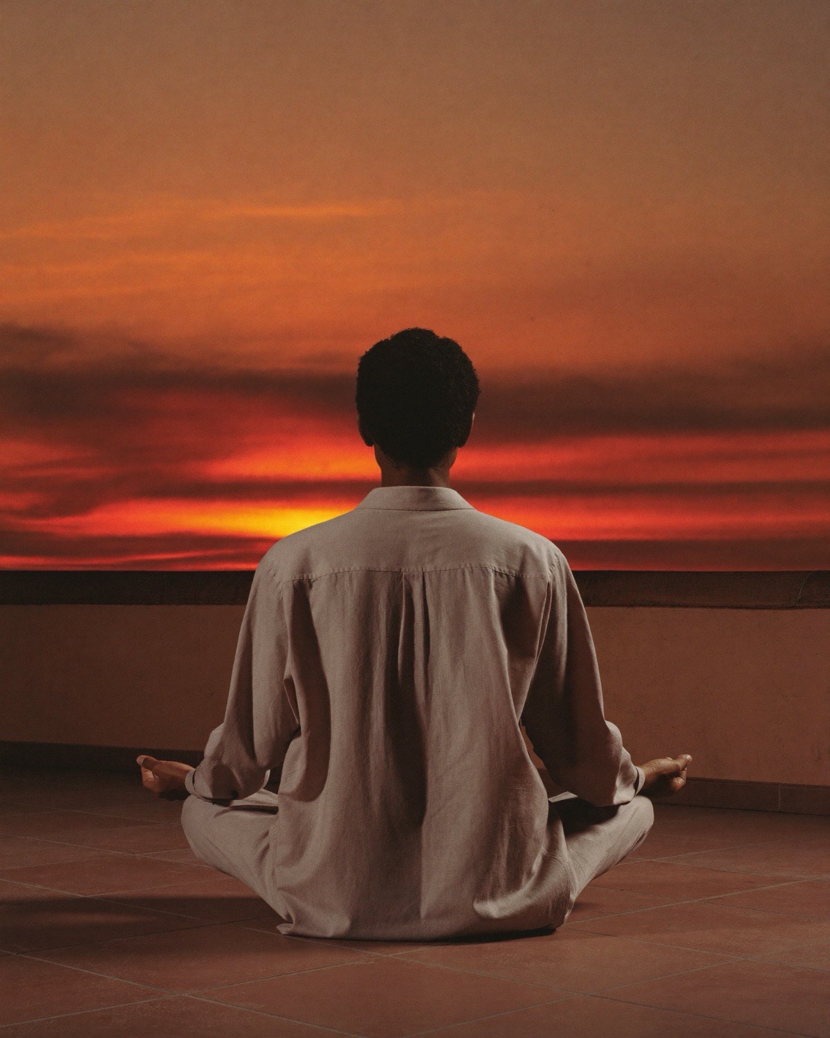 A person seated in meditation, facing a warm sunset over a terracotta rooftop terrace